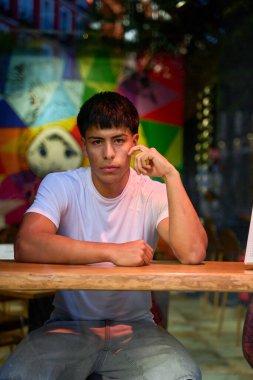 Kafe masasında oturan genç Latin adam ciddi bir ifadeyle