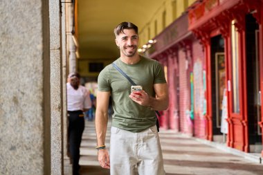 Şehir ortamında yürürken akıllı telefon kullanan gülümseyen adam