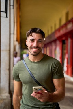 Şehir ortamında yürürken akıllı telefon kullanan gülümseyen adam