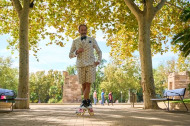Parkta patenlerle poz veren desenli takım elbiseli bir adam.
