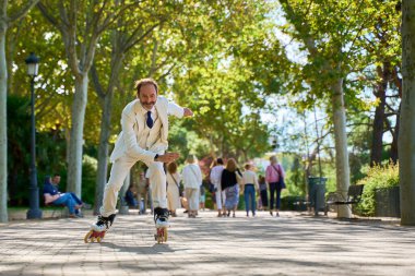 Takım elbiseli bir adam güneşli bir parkta neşeyle kayıyor.