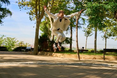 Güneşli bir parkta paten atlayan bir adam.