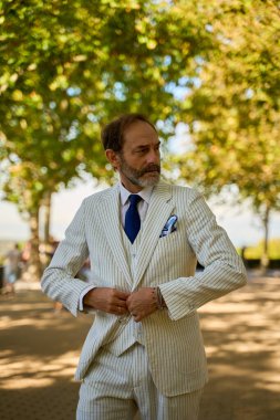 50 'den fazla beyaz adam güneşli parkta çizgili takım elbise giyiyor.