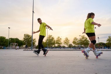 Erkek ve kadın gün batımında parkta senkronize paten antrenmanı yapıyorlar.