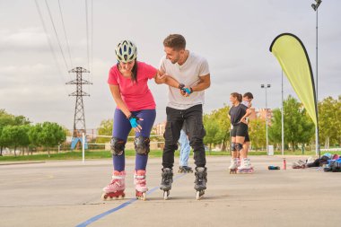 Erkek, bir kadına parkta paten çalışması için yardım ediyor.