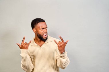 Heyecanlı genç adam bir el hareketiyle eğleniyor, müzik tutkusu ve neşe saçıyor. Havalı ve modaya uygun portre gençlik kültürünün ruhunu yansıtıyor.