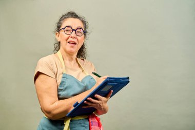 Mavi önlüklü kadın elinde bir dosya tutuyor ve gülümsüyor.