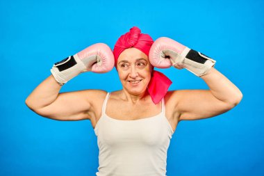 Kanserle mücadeleyi sembolize eden pembe boks eldiveni ve başörtüsü takmış kararlı olgun bir kadının stüdyo portresi