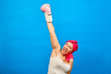 Pembe başörtülü güçlü orta yaşlı kadın boks eldivenli kolunu kaldırıyor, kanserle savaşıyor ve hastalıklara karşı zaferi kutluyor.