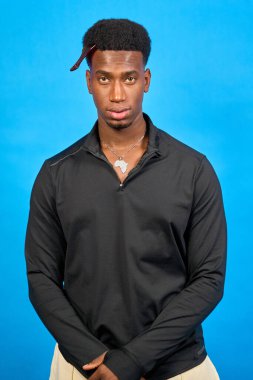 Mavi arka planda poz veren Afrika şekilli kolye giyen şık siyahi bir adamın stüdyo portresi.