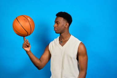 Genç sporcu parmak ucunda basketbol topunu çeviriyor, canlı mavi bir arka plana karşı yetenek ve konsantrasyon sergiliyor.
