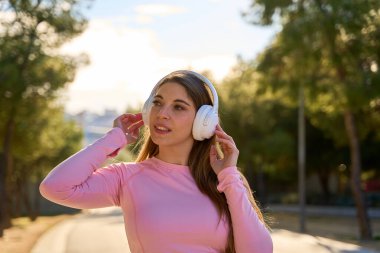 Güneşli bir parkta antrenman yaparken müziğin keyfini çıkaran mutlu bir sporcu, açık havayı kucaklıyor ve sağlıklı, aktif bir yaşam tarzını kutluyor.