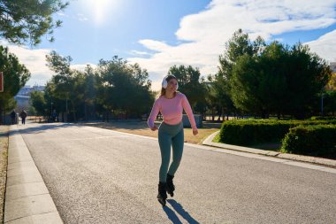 Parkta paten kayan, kulaklıkla müzik dinleyen, antrenman yapan ve güneşli bir günün tadını çıkaran zinde bir sporcu kadın.