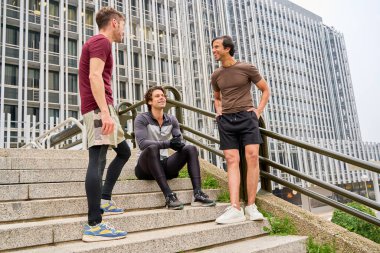 Üç erkek sporcu ara verip şehir basamaklarında sohbet ediyorlar. Açık havada egzersiz yaptıktan sonra arkadaşlığın tadını çıkarıyorlar.