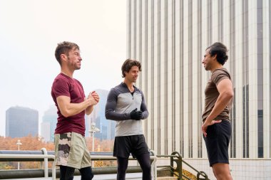 Üç erkek sporcu şehir ortamında eğitimlerini tartışıyor, arkadaşlığın ve fitness 'in tadını çıkarıyorlar.