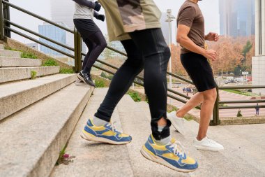 Modern kentsel bir ortamda eğitim sırasında merdivenlerden koşarak çıkan üç kişi, kararlılık ve takım çalışması sergiliyor.