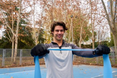 Genç bir sporcu, canlı bir sonbahar yeşillikleriyle çevrili bir şehir parkında elastik bir bantla egzersiz yapıyor ve sağlıklı bir yaşam tarzını kucaklıyor.