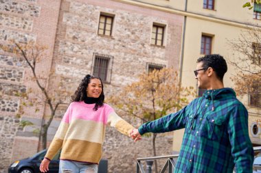 Şehir sokaklarında el ele yürüyen mutlu çoklu-etnik çift, birbirlerinin arkadaşlığından ve canlı kentsel atmosferden keyif alıyorlar.