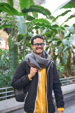 Genç adam kışlık giysiler giyiyor ve güzel botanik bahçelerini geziyor.