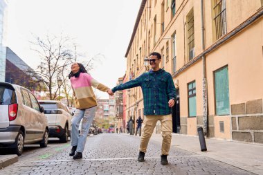 Cobblestone caddesinde neşeli bir şekilde yürürken el ele tutuşup gülen çok ırklı genç bir çift.