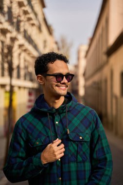 Yüzünde güneş gözlüğü ve kapüşonlu gömlek olan gülümseyen genç bir adamın portresi.