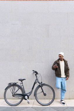 Bisikletinin yanındaki duvara yaslanırken akıllı telefon kullanan genç bir adam, şehir ortamında bir anlık bağlantının keyfini çıkarıyor.