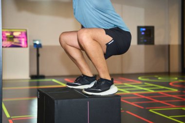 Sporcu, spor salonunda bir kutu atlayışı gerçekleştiriyor, dayanıklılık ve çeviklik eğitimine odaklanıyor ve neon kaplı zemini rehberlik için kullanıyor.