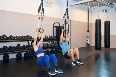 Modern bir spor salonunda jimnastik yapan iki kişi, iyi donanımlı bir çalışma alanının ortasında güç ve dayanıklılığa odaklanıyor.