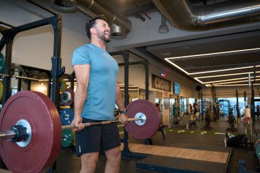 Çağdaş bir spor salonunda halter kaldıran adam spor ekipmanlarının arasında güç ve zindelik gösterisi yapıyor.
