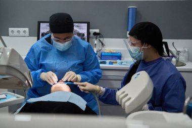 Dişçi ve asistanı, modern bir diş kliniğinde bir hastaya diş tedavisi uyguluyorlar.