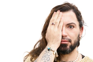 Sakallı bir Latin transseksüelin portresi. Uzun saçlı, sağ gözü beyaz bir arka planda.