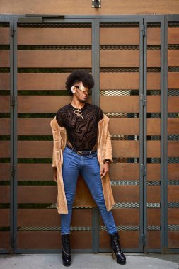 Afro saçlı, şık giyinen ve şehir ortamında poz veren modaya uygun olmayan biri.