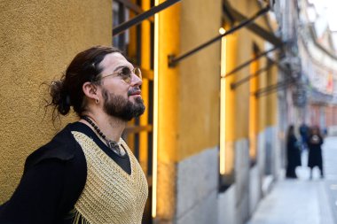 Uzun saçlı ve sakallı şık olmayan biri, şehir sokaklarında poz verirken başka tarafa bakıyor.