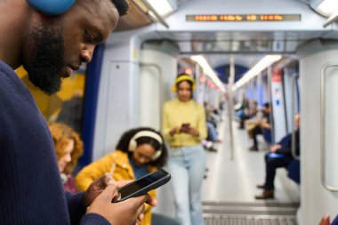 Genç banliyö çalışanı kulaklıkla müzik dinlerken ve metroyla seyahat ederken cep telefonu kullanıyor.