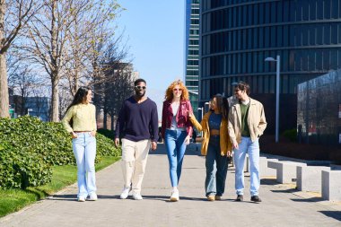 Modern bir şehir parkında birlikte yürüyüp sohbet eden beş genç etnik arkadaş, boş zamanlarının tadını çıkarıyorlar.