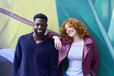 Mutlu çok ırklı çift gülümsüyor ve renkli bir duvar yazısı karşısında birlikte poz veriyorlar.