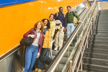 Çantalı ve kulaklıklı bir grup öğrenci üniversiteden sonra metro istasyonunda yürüyen merdivenle yükselecek.
