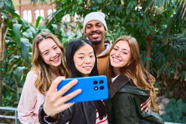 Dört neşeli arkadaş yemyeşil bir ortamda birlikte neşeli bir selfie çekiyorlar, doğanın ortasında dostluk ve mutluluk sergiliyorlar.