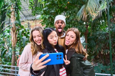 Bir grup arkadaş birlikte eğlenceli bir anın tadını çıkarıyorlar. Bereketli bir tropik serada selfie çekiyorlar. Etrafı canlı yeşilliklerle çevrili.
