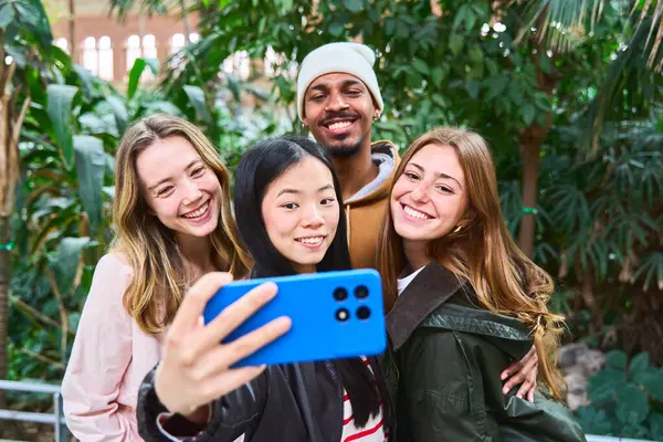 Dört neşeli arkadaş yemyeşil bir ortamda birlikte neşeli bir selfie çekiyorlar, doğanın ortasında dostluk ve mutluluk sergiliyorlar.