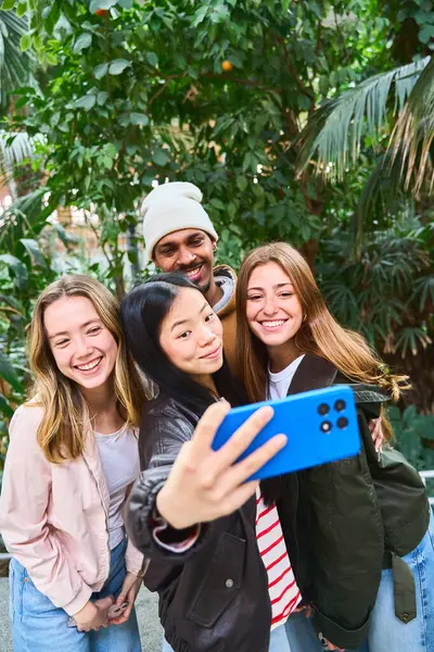 Dört neşeli çoklu etnik öğrenci botanik bahçesinde akıllı bir telefonla selfie çekiyor ve birlikte boş zamanlarının tadını çıkarıyorlar.