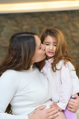 Latin hamile anne kızını öperken çocuk büyüyen karnını nazikçe okşuyor, sevgi ve bağlılık anını paylaşıyor.