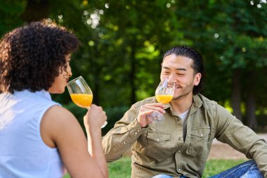 Şarap kadehlerinde portakal suyu içen, parkta yaz pikniğinin tadını çıkaran çok ırklı genç bir çift.