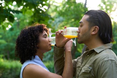 Parkta gözlüklerden portakal suyu içen ırklar arası bir çift doğayla çevrili romantik bir anın tadını çıkarıyor.