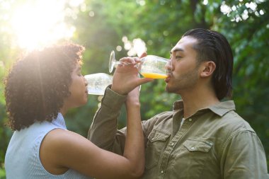 Irklar arası genç çift şarap kadehlerinden ferahlatıcı meyve suyu içiyor, güneşli bir günün tadını çıkarıyorlar, doğayla iç içe.