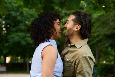 Doğanın güzellikleriyle çevrili canlı yeşil bir parkta gülen ve neşeli bir romantik anı paylaşan çok ırklı genç bir çift.