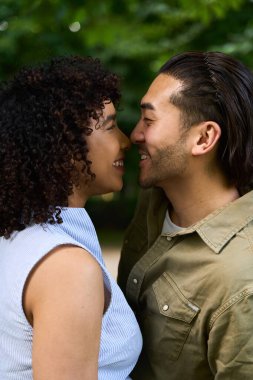 Genç çoklu etnik çift dışarıda romantik bir an yaşıyor, gülümsüyor ve parkta öpüşmek üzereler.