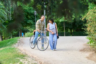 İki genç iş arkadaşı mola veriyor, yeşil bir parkta yürüyor ve bisiklete biniyor, dizüstü bilgisayar tutuyor ve gülümsüyor.