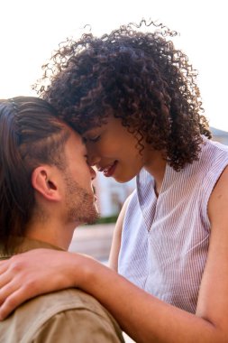 Romantik çift alınlarına dokunuyor, açık havada hassas bir anın tadını çıkarıyor, sıcak yaz güneşinin altında sevgi ve samimiyet yayıyor.