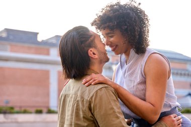 Genç çok ırklı çift açık havada hassas bir anı paylaşıyor, birbirlerine sevgi ve sevgiyle sarılıp gülümsüyorlar.